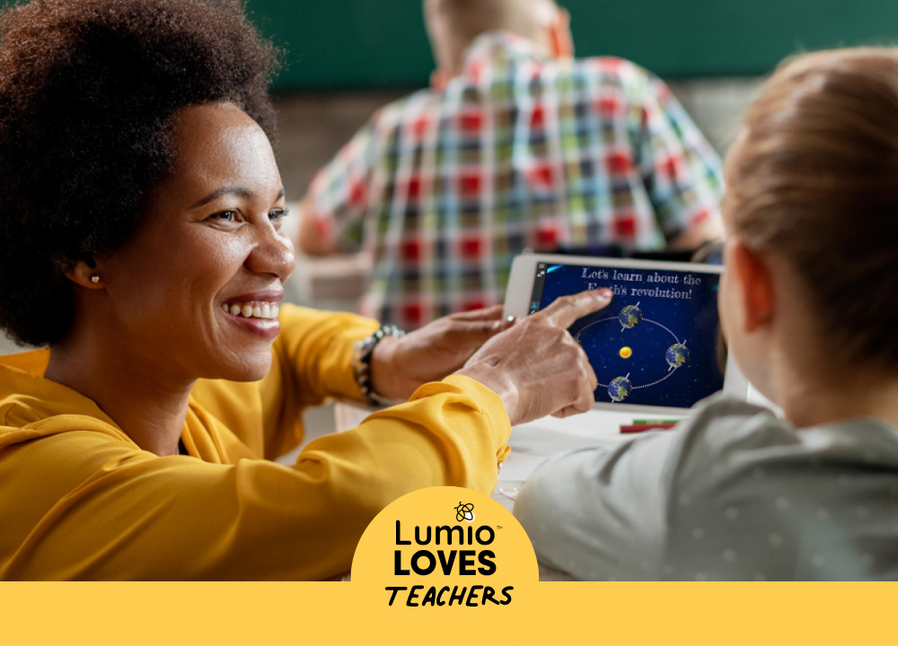 A female teacher wearing a yellow blouse talks with her student and smiles while pointing to a tablet displaying Lumio